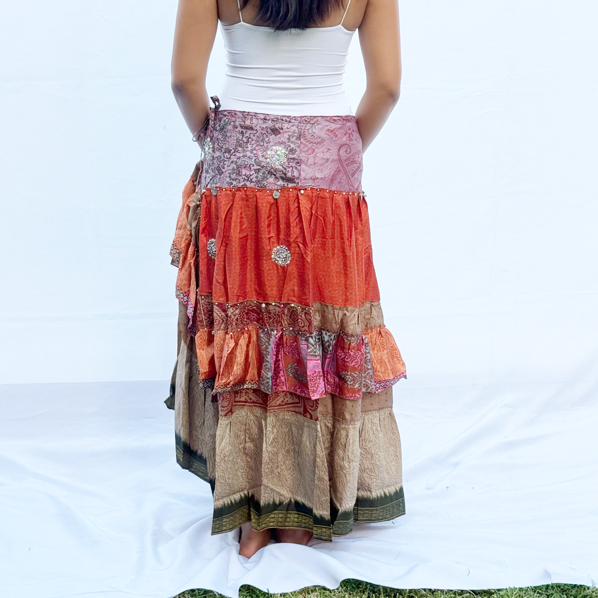  A vibrant patchwork skirt made from vintage saris, featuring shades of orange, pink, beige, and green with intricate patterns. The skirt includes an adjustable drawstring for a customisable fit.