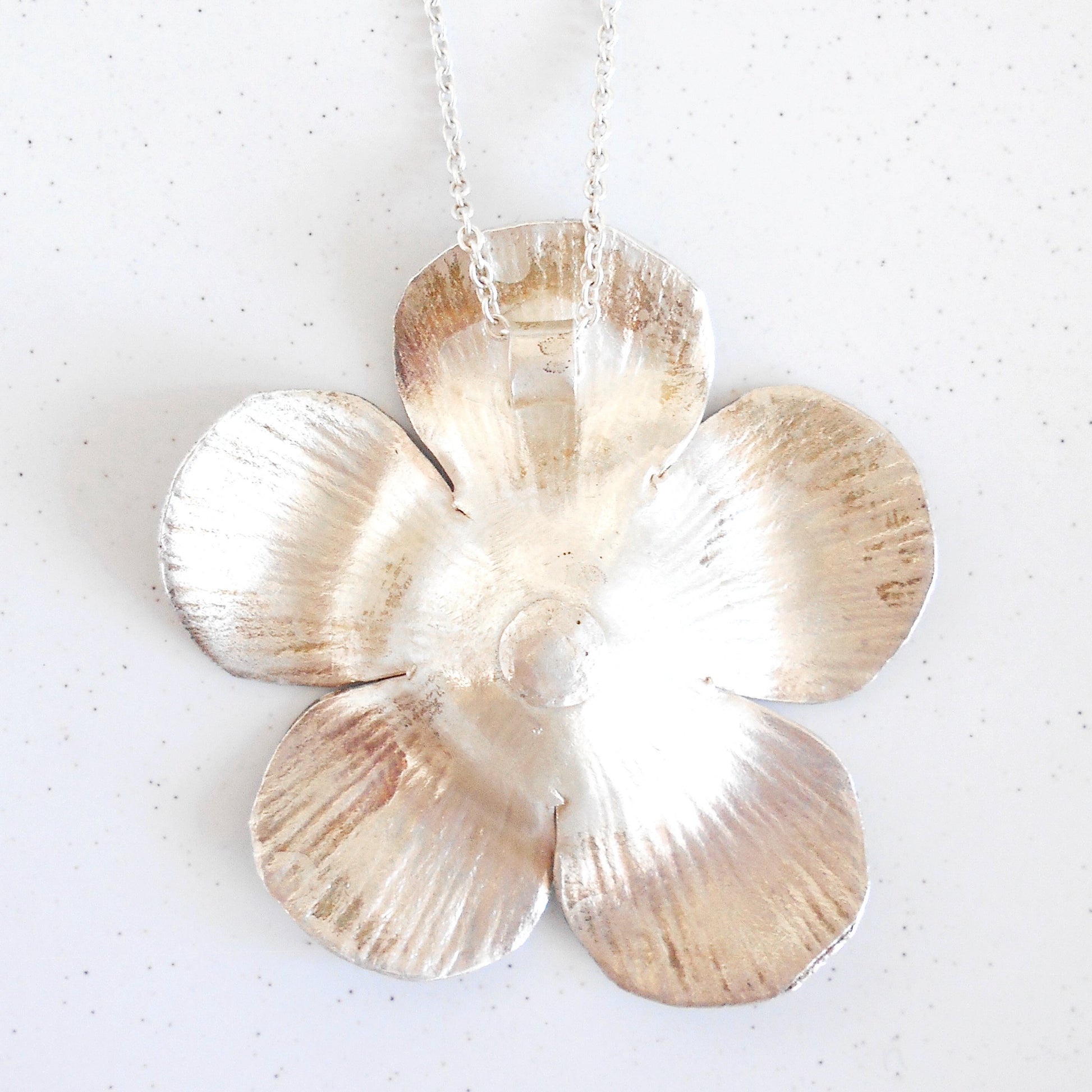 Close-up of a large Vintage Sterling Silver flower pendant necklace being worn. Pendant features textured petals and silver bead details in the center, hanging on a silver chain. Handcrafted by Nepalese artisans for Dilmaya Gifts.
